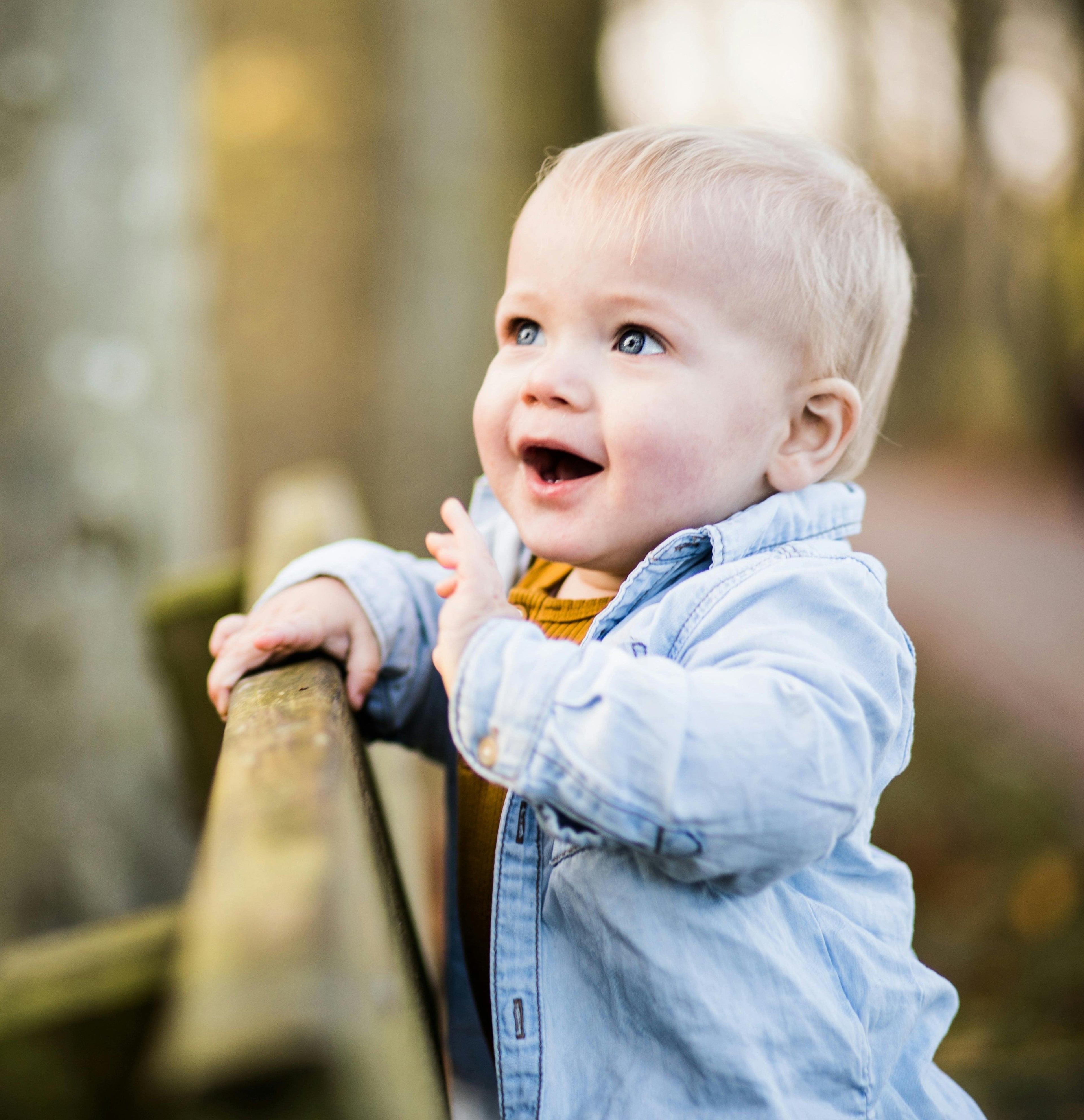 Baby boy outside in a forest, smiling and waving in sunshine.
