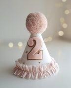 White party hat with pink number '2' and pom-pom on a blurred light background.
