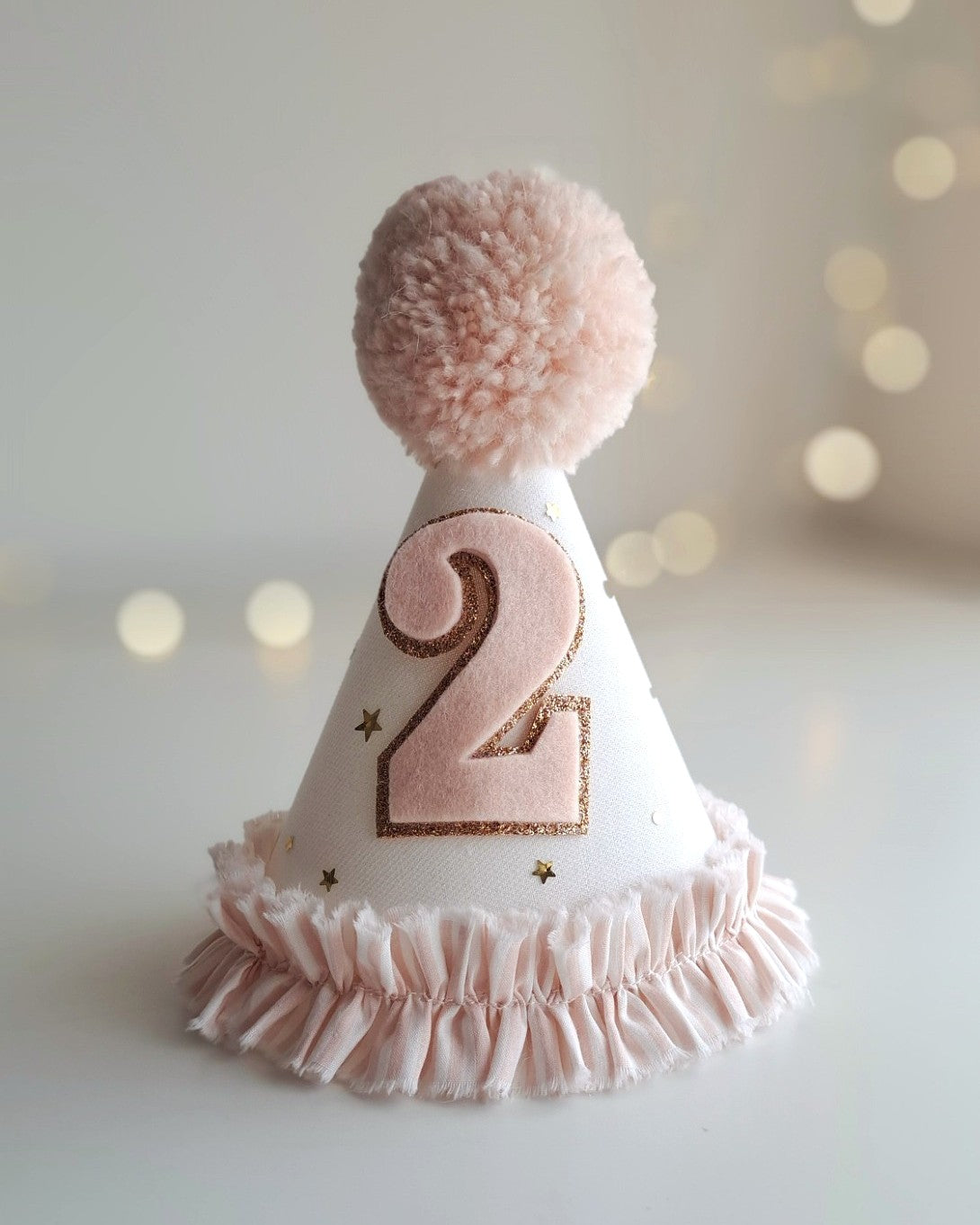 White party hat with pink number '2' and pom-pom on a blurred light background.