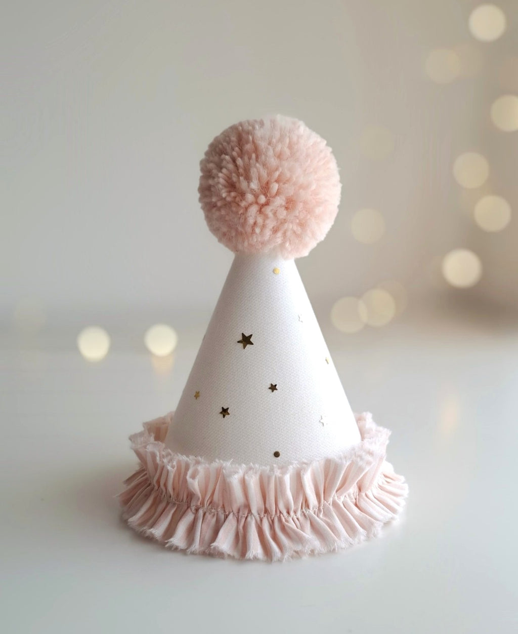 White party hat with pink pom-pom and ruffle on a light background.