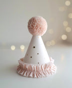 White party hat with pink pom-pom and ruffle on a light background.