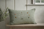 Green pillow with embroidered name and decorative elements on a wooden bench - personalised baby / toddler gift.