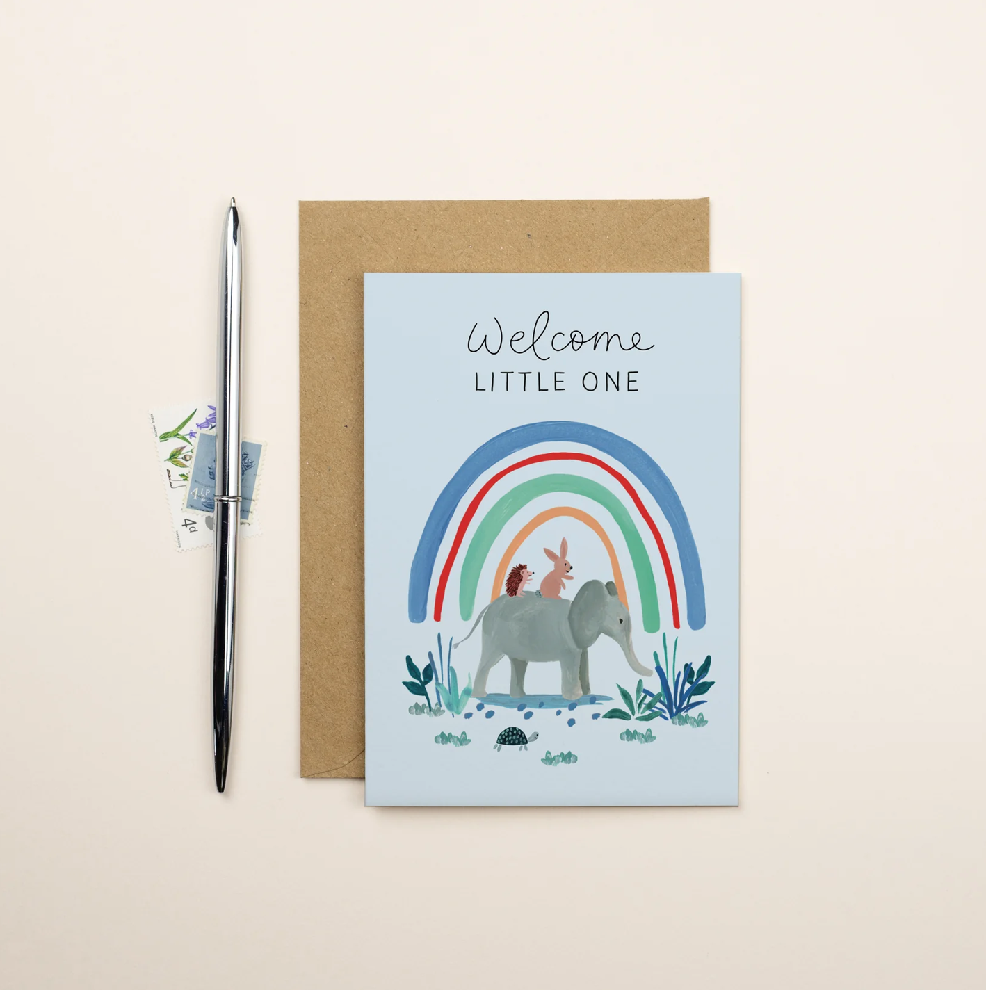 Greeting card with illustration of a rainbow, elephant, and deer with 'Welcome Little One' text on a beige background.