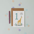 Greeting card with a giraffe illustration and 'One Today' text, placed on a light blue background with polka dots.