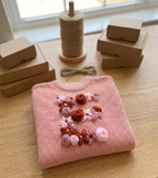Pink sweater with floral embellishments on a wooden surface