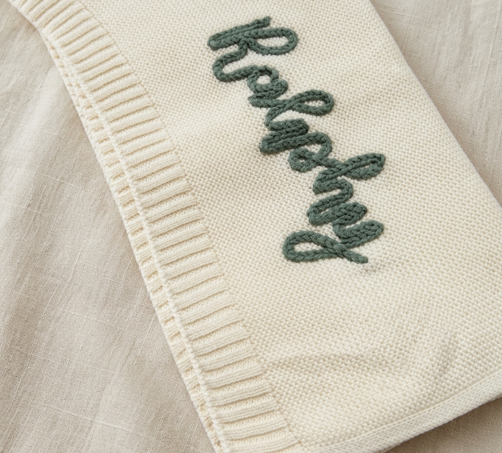 Cream-colored blanket with green embroidered text on a beige background -  personalised gift.
