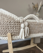 Beige woven basket with tassels on a wooden stand against a neutral background.