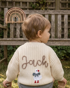 Child wearing a beige cardigan with name and a snowman design, standing outdoors  -  personalised baby / toddler gift.