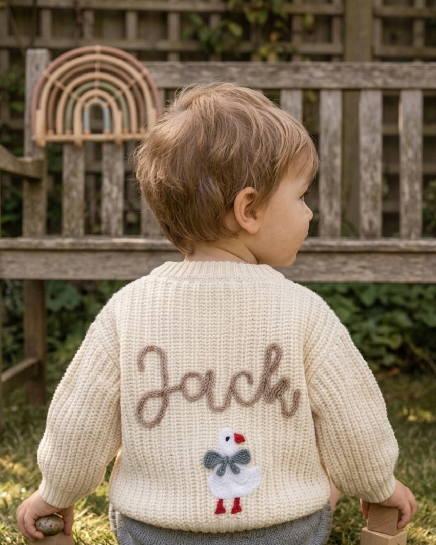 Child wearing a beige cardigan with name and a snowman design, standing outdoors  -  personalised baby / toddler gift.