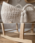 Knitted mosses basket with tassels on a wooden stand.