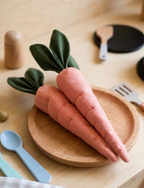 Knitted toy carrots on a wooden plate with utensils in the background.