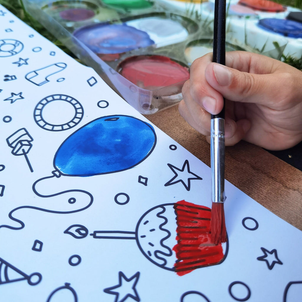 Hand holding a paintbrush over a coloring book with blue and red paint.