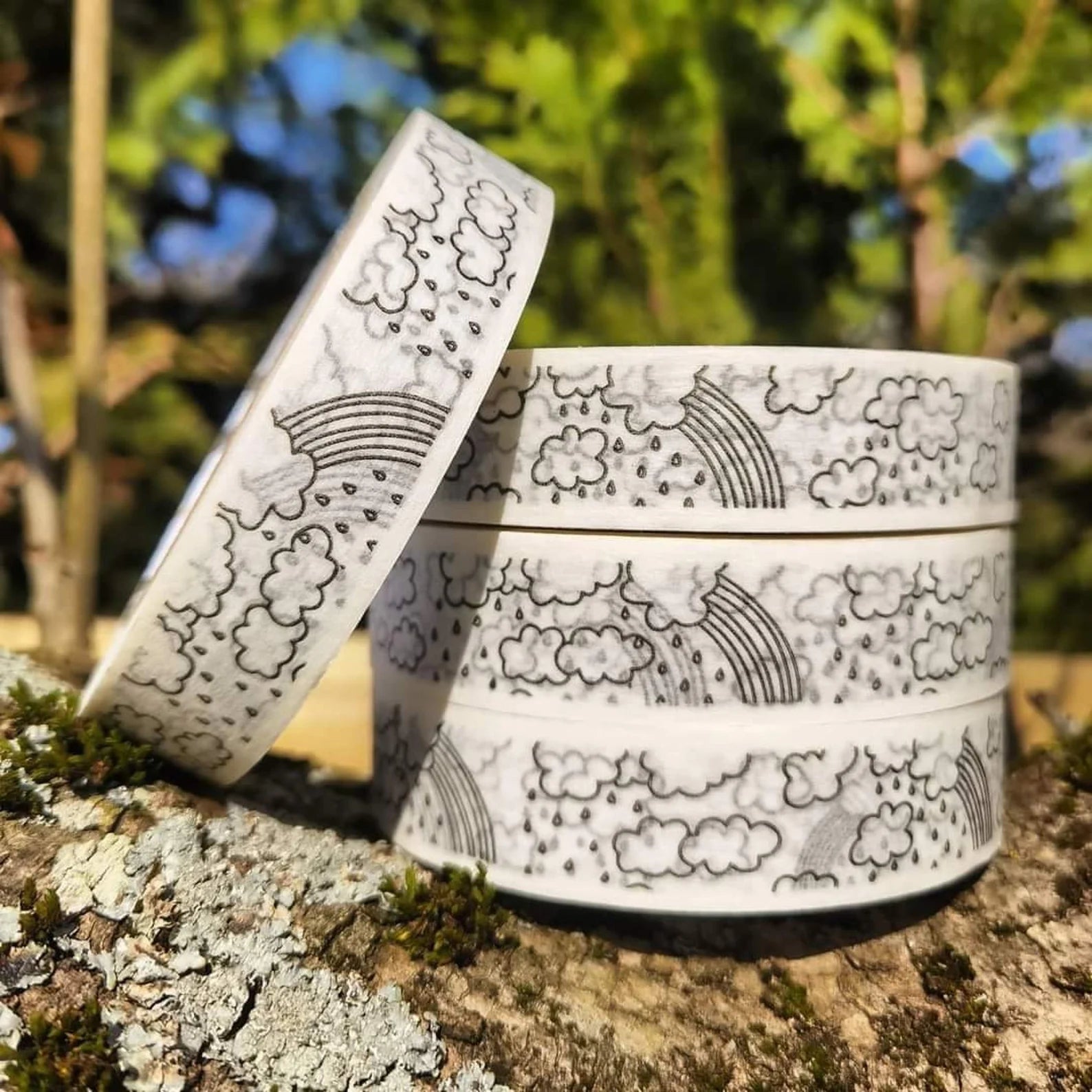 Two cylindrical containers with cloud and rainbow patterns on a natural background