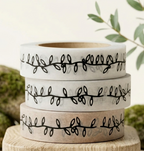 Three rolls of washi tape with black leaf patterns on a wooden block with a natural background.