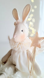 Stuffed bunny toy in a white dress holding a star, with a soft focus background- heirloom baby/toddler gifts.