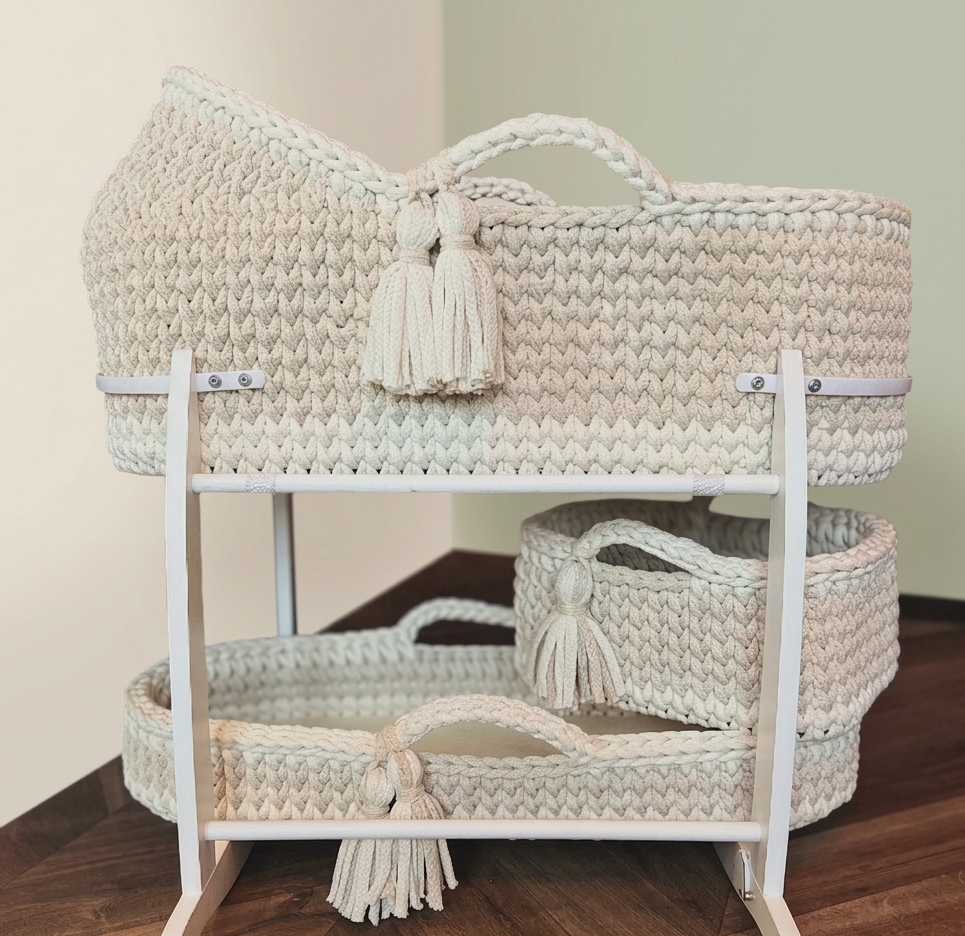 Woven baby bassinet with tassels on a wooden floor against a beige wall
