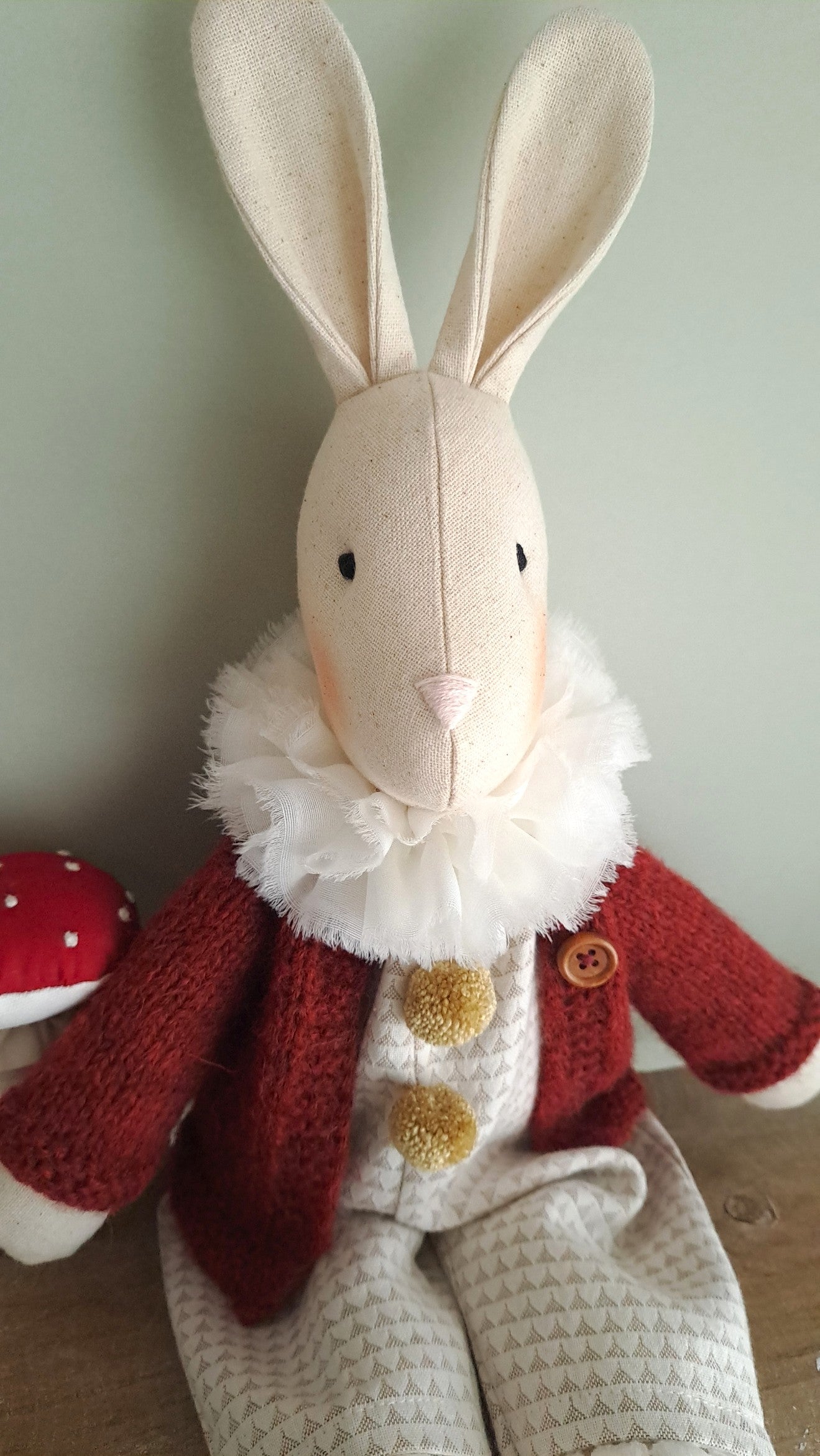 Stuffed rabbit toy wearing a red coat with gold buttons on a light background- heirloom baby/toddler gifts.