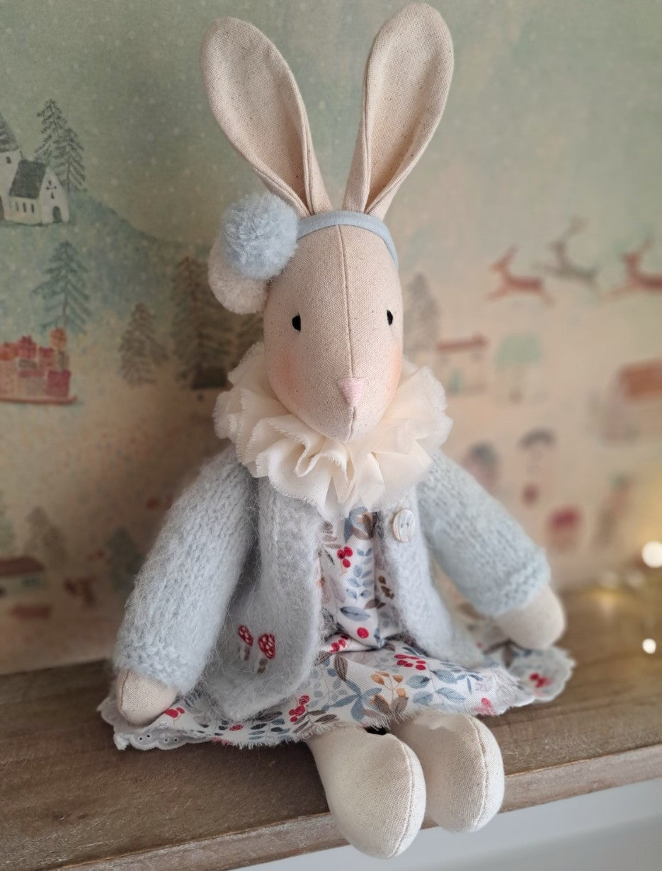 Stuffed rabbit toy with a floral dress and grey coat on a wooden surface- heirloom baby/toddler gifts.