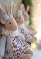 Three plush bunny toys in dresses with a blurred background- heirloom baby/toddler gifts.